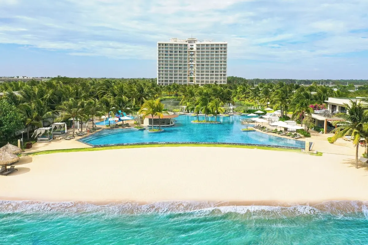 Resort có hồ bơi lớn giữa vườn dừa, phía trước là bãi cát trắng và biển xanh