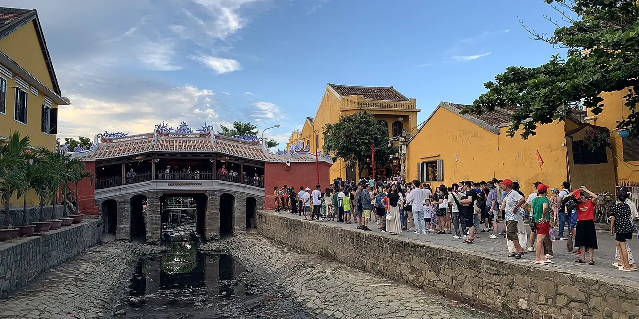 Chùa Cầu mái ngói mũi hài bắc qua lạch nước, hai bên là nhà tường vàng và dòng du khách